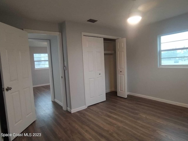 unfurnished bedroom with dark wood-style floors, a closet, visible vents, and baseboards