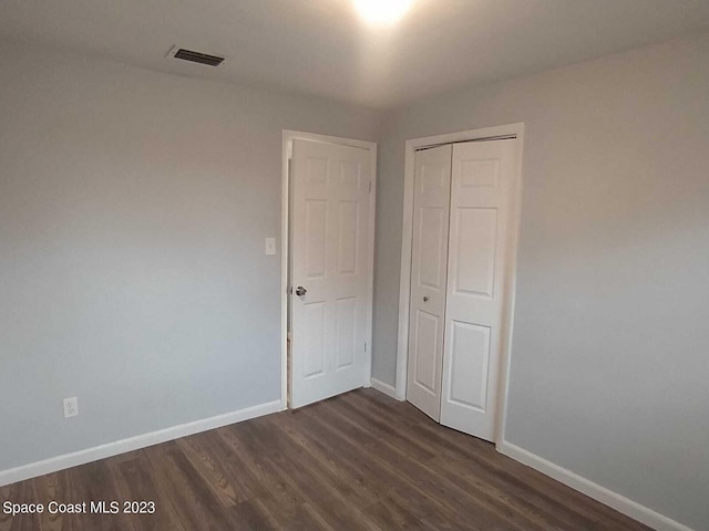 unfurnished bedroom with dark wood-style floors, visible vents, baseboards, and a closet