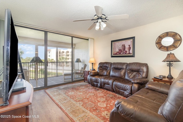 living room featuring ceiling fan, a textured ceiling, a wall of windows, and wood finished floors