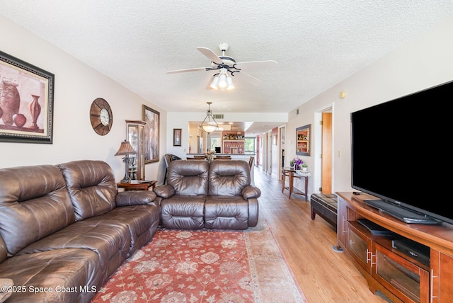 living room featuring light wood-type flooring, visible vents, ceiling fan, and a textured ceiling