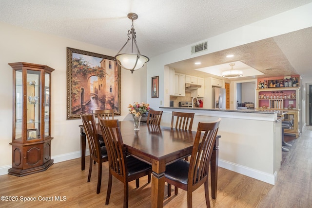 dining area with baseboards, light wood-style flooring, visible vents, and a textured ceiling