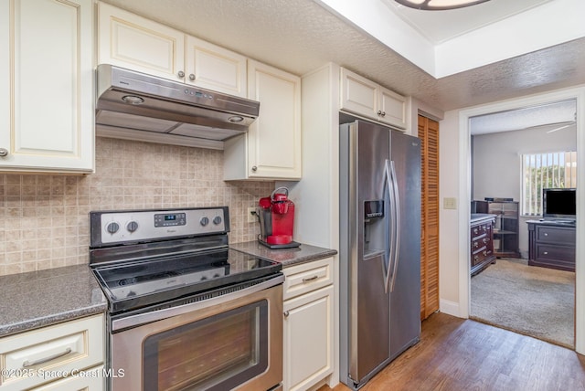 kitchen featuring under cabinet range hood, light wood-style floors, appliances with stainless steel finishes, decorative backsplash, and dark countertops