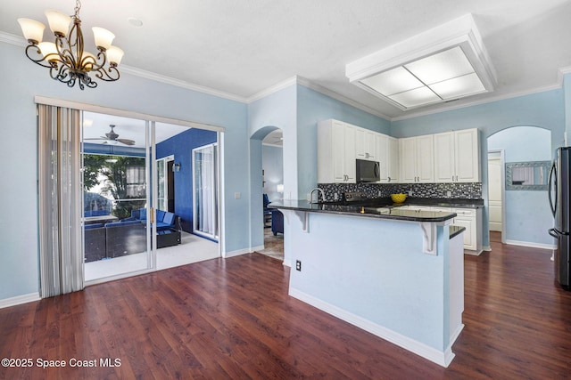 kitchen with dark countertops, black microwave, arched walkways, and a breakfast bar