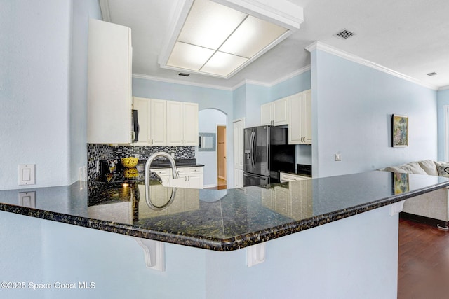 kitchen featuring ornamental molding, a peninsula, black refrigerator with ice dispenser, and visible vents