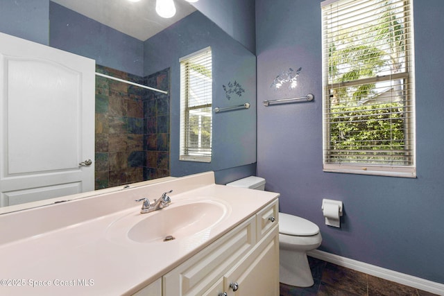 full bathroom featuring tiled shower, vanity, toilet, and baseboards