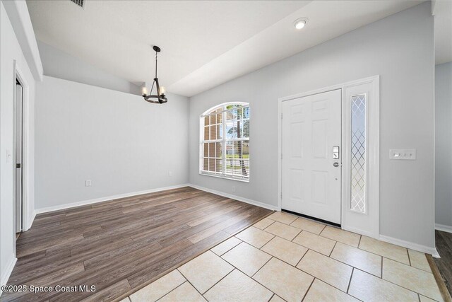 entryway featuring lofted ceiling, an inviting chandelier, baseboards, and wood finished floors