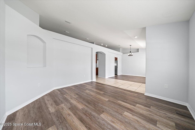 unfurnished room featuring baseboards, visible vents, arched walkways, and wood finished floors