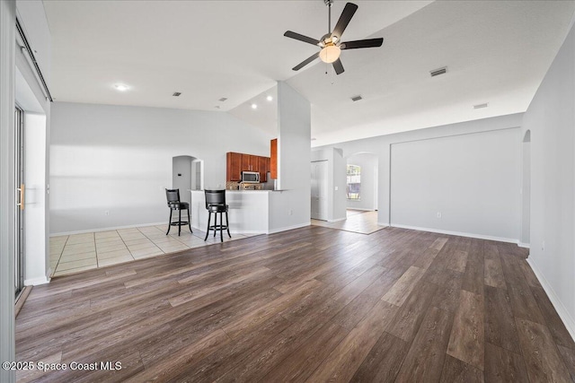 unfurnished living room featuring arched walkways, ceiling fan, lofted ceiling, wood finished floors, and baseboards