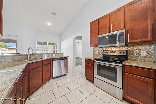 kitchen featuring light tile patterned floors, stainless steel appliances, backsplash, a sink, and light stone countertops