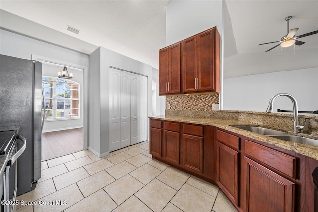 kitchen featuring visible vents, light stone counters, a sink, backsplash, and ceiling fan with notable chandelier