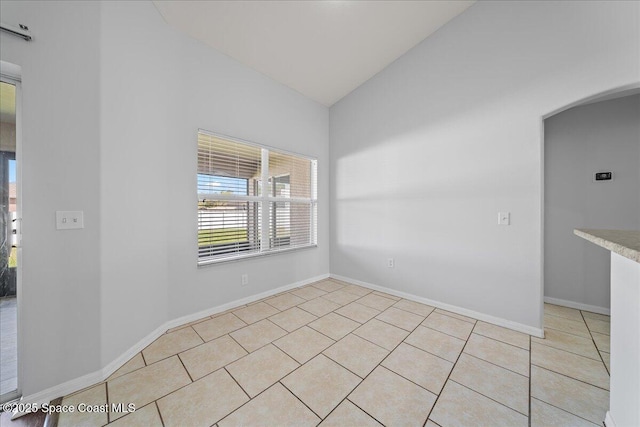 empty room with light tile patterned floors, arched walkways, lofted ceiling, and baseboards