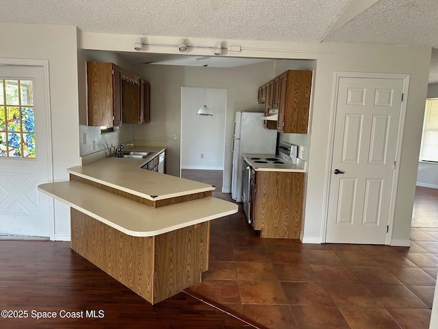 kitchen with white range with electric stovetop, brown cabinets, a peninsula, light countertops, and a sink