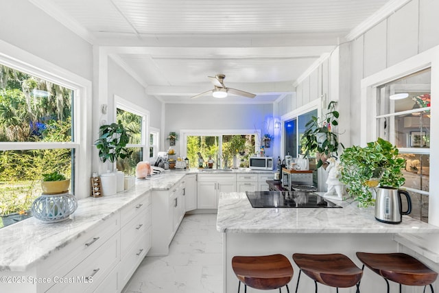 kitchen with black electric stovetop, a breakfast bar area, light stone counters, white cabinets, and marble finish floor