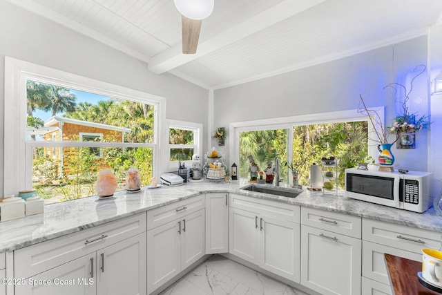 kitchen featuring marble finish floor, beam ceiling, white microwave, white cabinets, and a sink