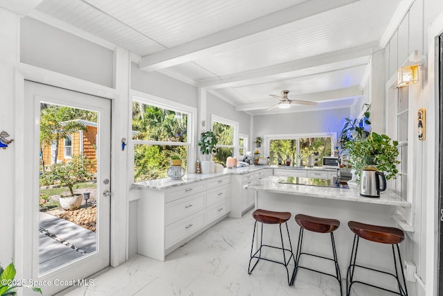 sunroom with plenty of natural light, a ceiling fan, and beamed ceiling