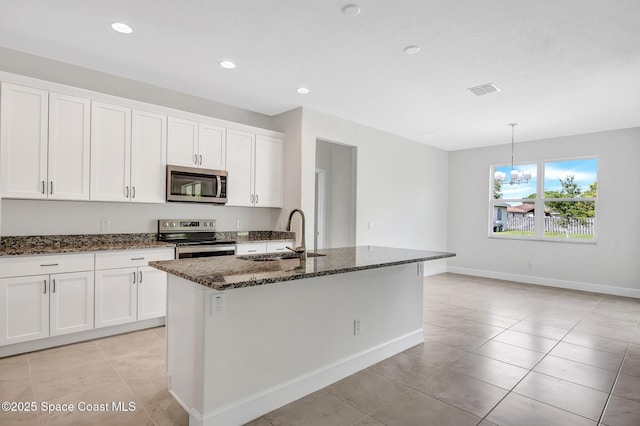 kitchen with a kitchen island with sink, stainless steel appliances, a sink, white cabinetry, and dark stone countertops