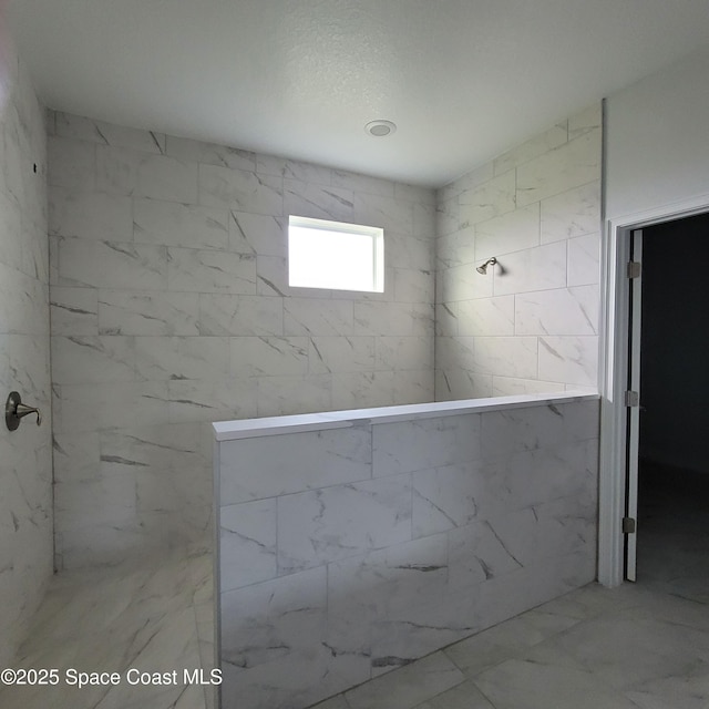 bathroom featuring marble finish floor and a tile shower