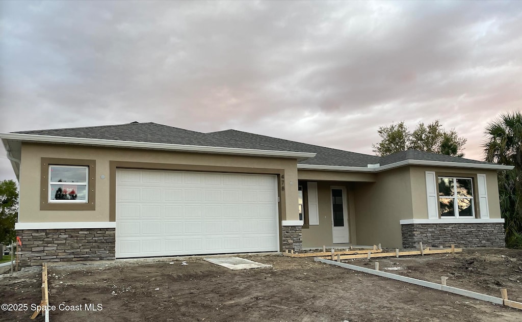 prairie-style home featuring an attached garage, stone siding, roof with shingles, and stucco siding