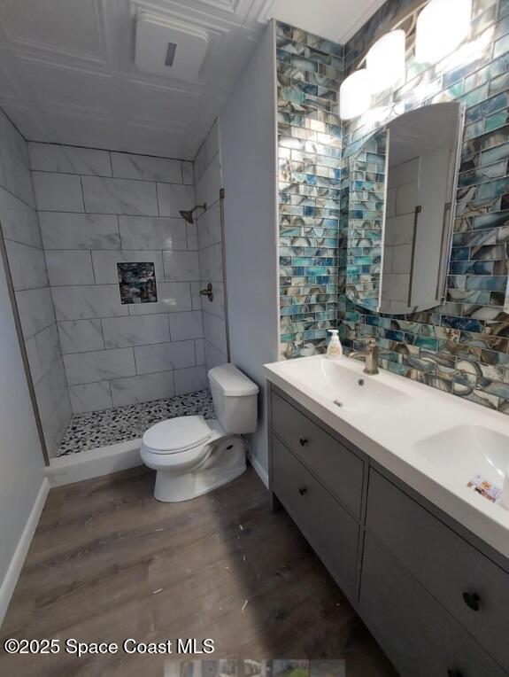 bathroom with toilet, double vanity, tiled shower, and wood finished floors