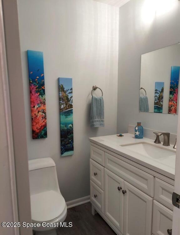 half bathroom featuring toilet, baseboards, wood finished floors, and vanity