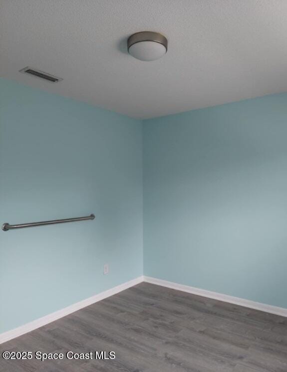 empty room featuring baseboards, a textured ceiling, visible vents, and dark wood-type flooring