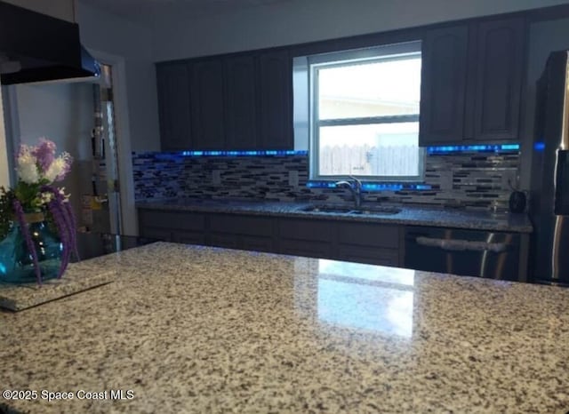 kitchen featuring dishwasher, a sink, light stone countertops, and decorative backsplash