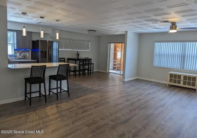 kitchen with dark wood-style flooring, baseboards, stainless steel fridge, a peninsula, and a kitchen bar