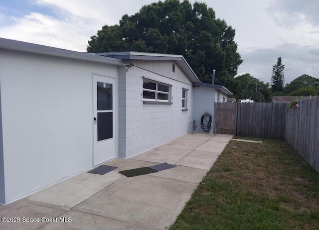 view of side of home featuring a gate, concrete block siding, fence, and a patio