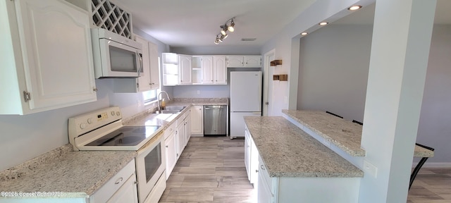 kitchen with rail lighting, white appliances, white cabinetry, and a sink