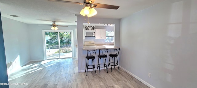 kitchen featuring white microwave, a breakfast bar area, stove, white cabinetry, and plenty of natural light