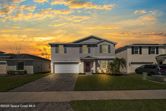 traditional home with decorative driveway, an attached garage, a lawn, and stucco siding