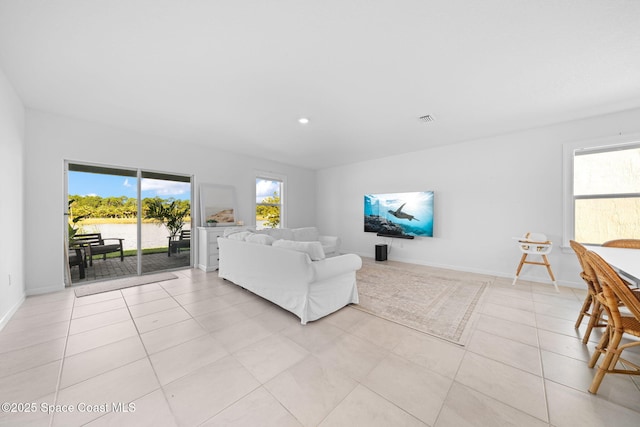 living area featuring light tile patterned floors, baseboards, visible vents, and a healthy amount of sunlight