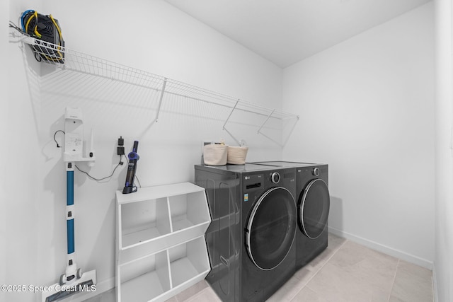 clothes washing area featuring laundry area, tile patterned floors, washing machine and clothes dryer, and baseboards