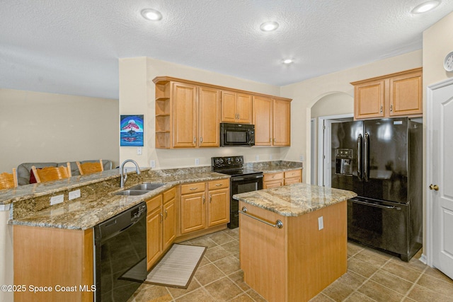 kitchen with light stone counters, a peninsula, black appliances, open shelves, and a sink