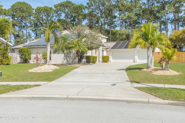 view of front of home featuring an attached garage, roof mounted solar panels, fence, driveway, and a front lawn