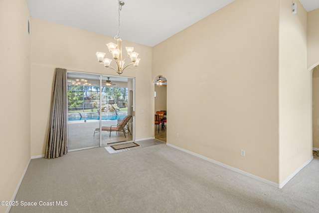 carpeted empty room with arched walkways, a notable chandelier, a towering ceiling, and baseboards