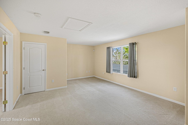 carpeted empty room with attic access, visible vents, a textured ceiling, and baseboards