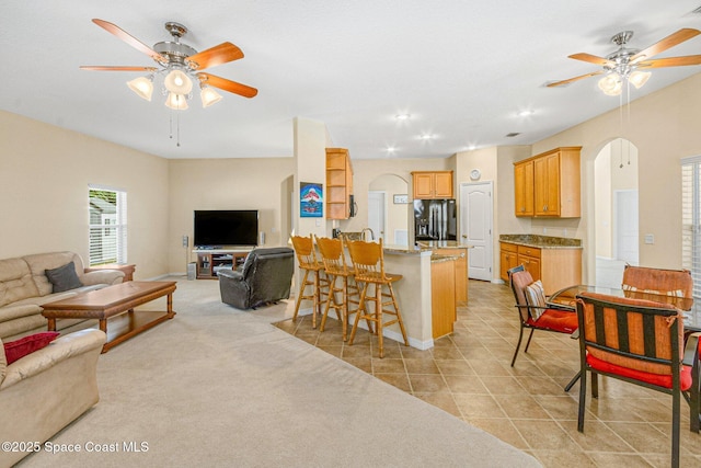 living area featuring arched walkways, light tile patterned floors, light carpet, and a ceiling fan