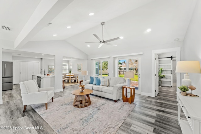 living room featuring a barn door, visible vents, baseboards, vaulted ceiling, and light wood-type flooring