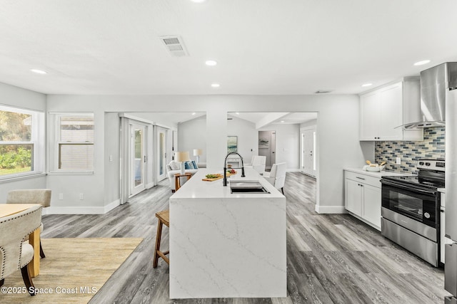 kitchen with stainless steel electric stove, a sink, visible vents, wall chimney range hood, and decorative backsplash