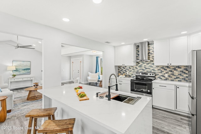 kitchen featuring stainless steel appliances, a sink, a kitchen breakfast bar, wall chimney range hood, and tasteful backsplash