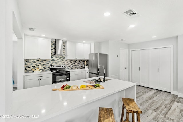 kitchen with visible vents, electric range, freestanding refrigerator, a sink, and wall chimney range hood