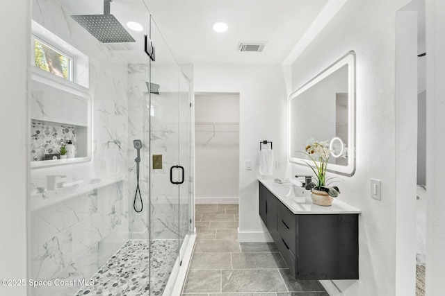 full bathroom featuring visible vents, baseboards, a marble finish shower, double vanity, and a walk in closet