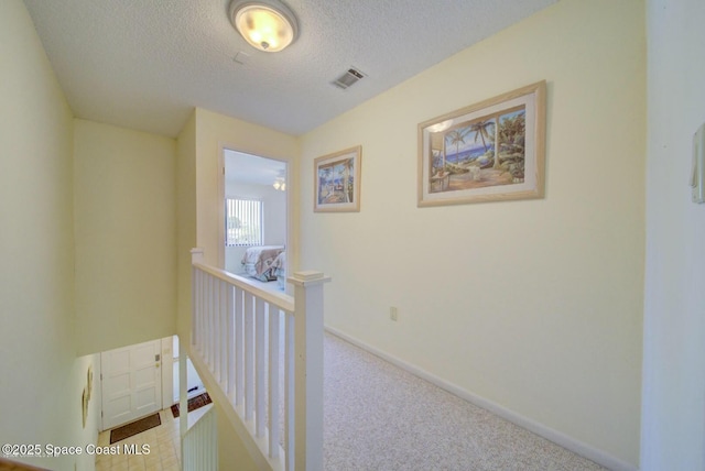 hallway with baseboards, visible vents, an upstairs landing, a textured ceiling, and carpet flooring