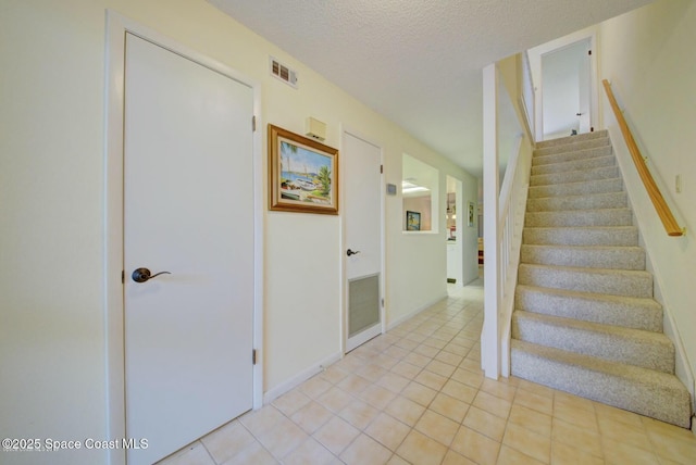 stairs featuring tile patterned flooring, visible vents, and a textured ceiling