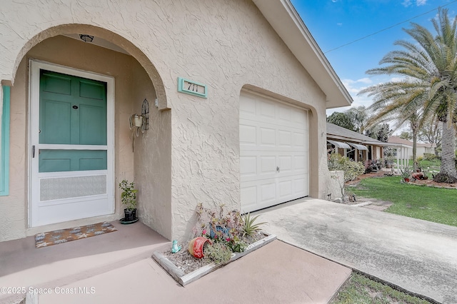 view of exterior entry featuring a garage, driveway, and stucco siding