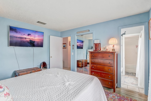 bedroom with a closet, visible vents, ensuite bathroom, a textured ceiling, and wood finished floors