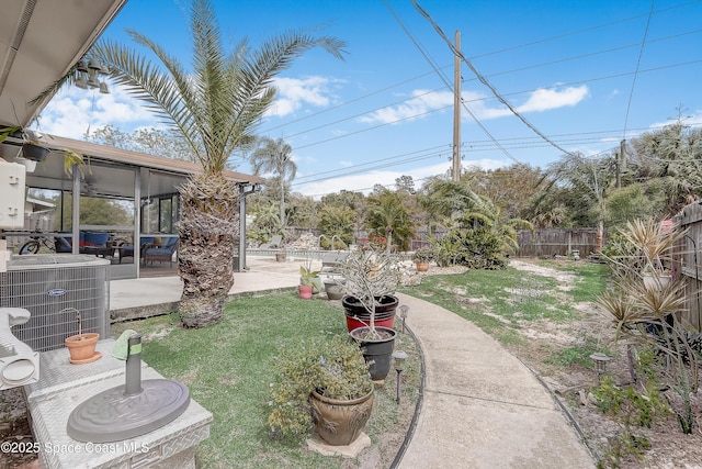 view of yard featuring a sunroom, a fenced backyard, a patio, and central AC