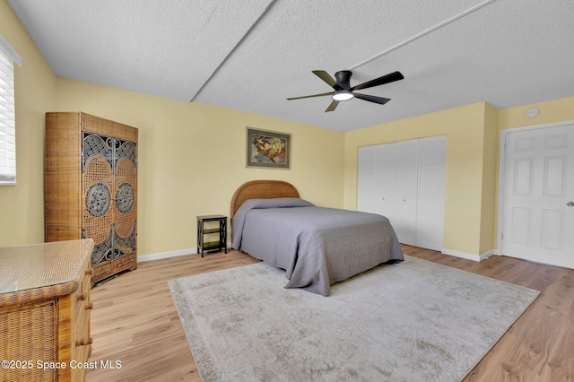 bedroom with a closet, baseboards, a textured ceiling, and light wood-style flooring