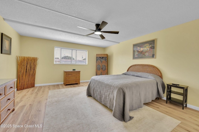 bedroom with light wood-style flooring, a ceiling fan, baseboards, and a textured ceiling